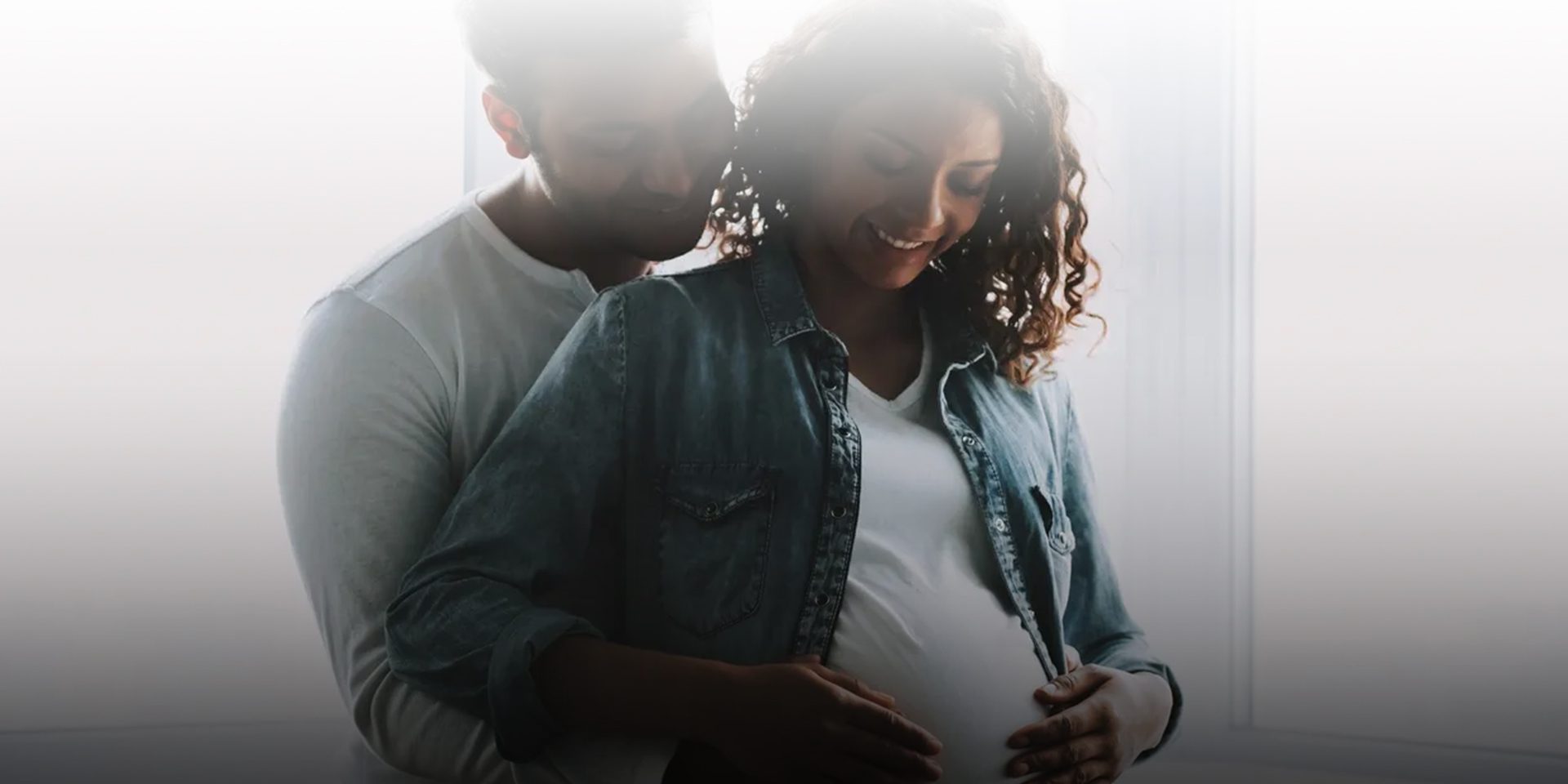 Expectant couple embracing, hands on pregnant belly