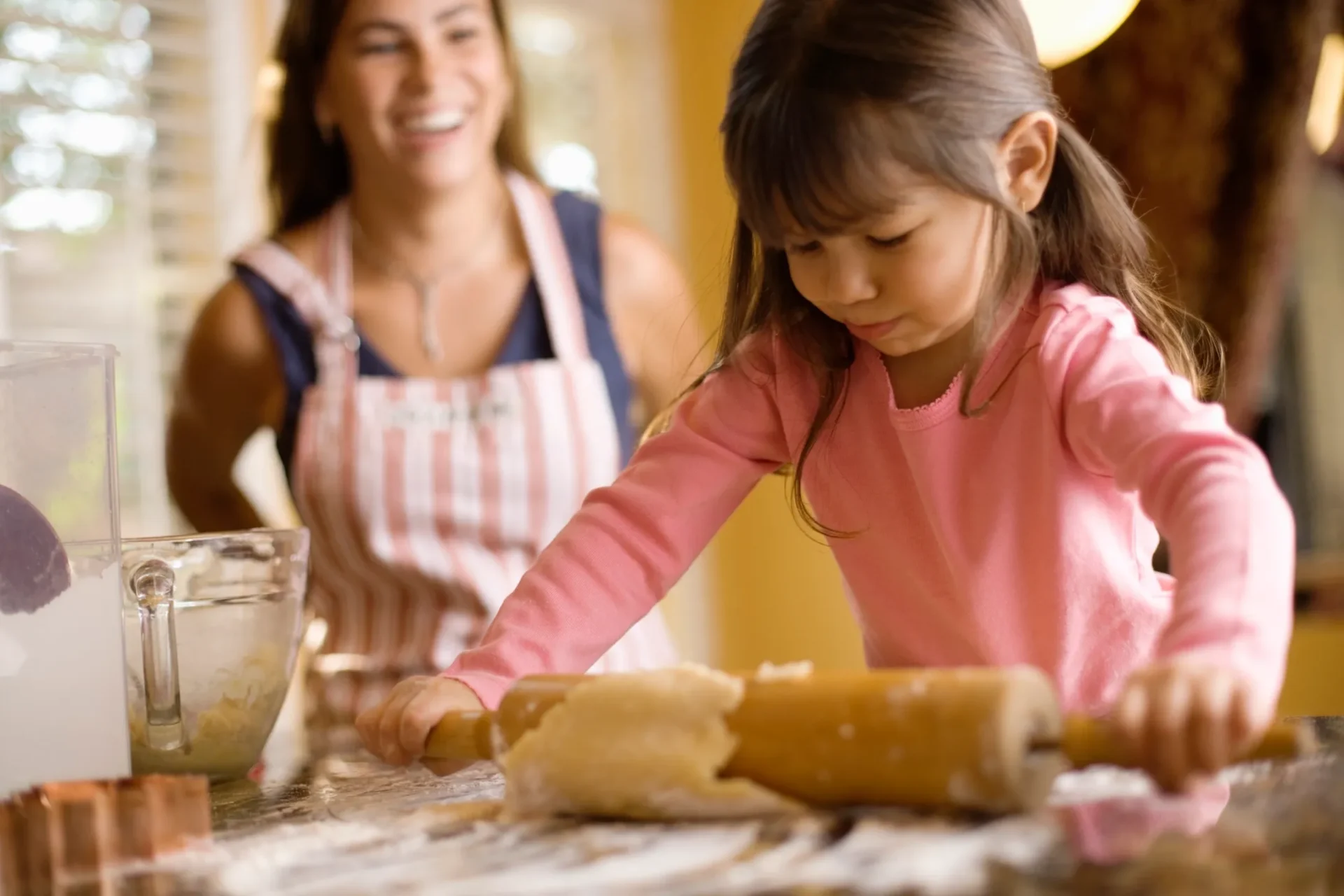 Child rolling dough while mother watches