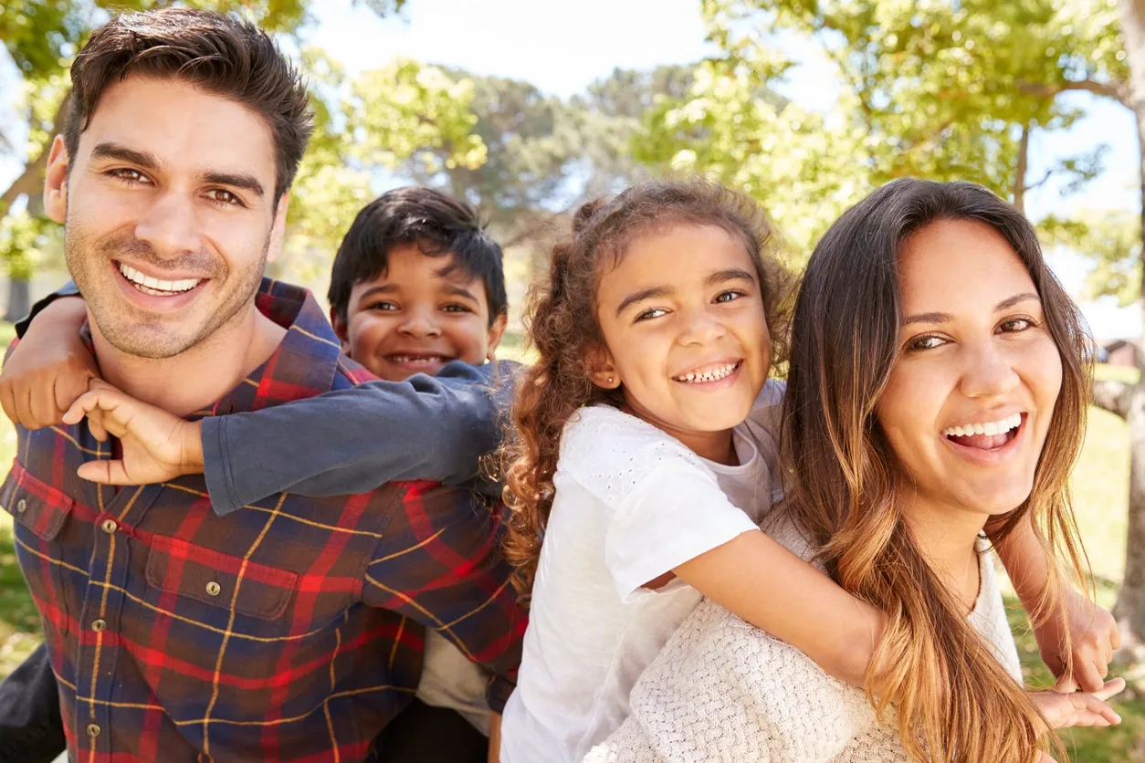 Smiling family of four outdoors, kids piggyback